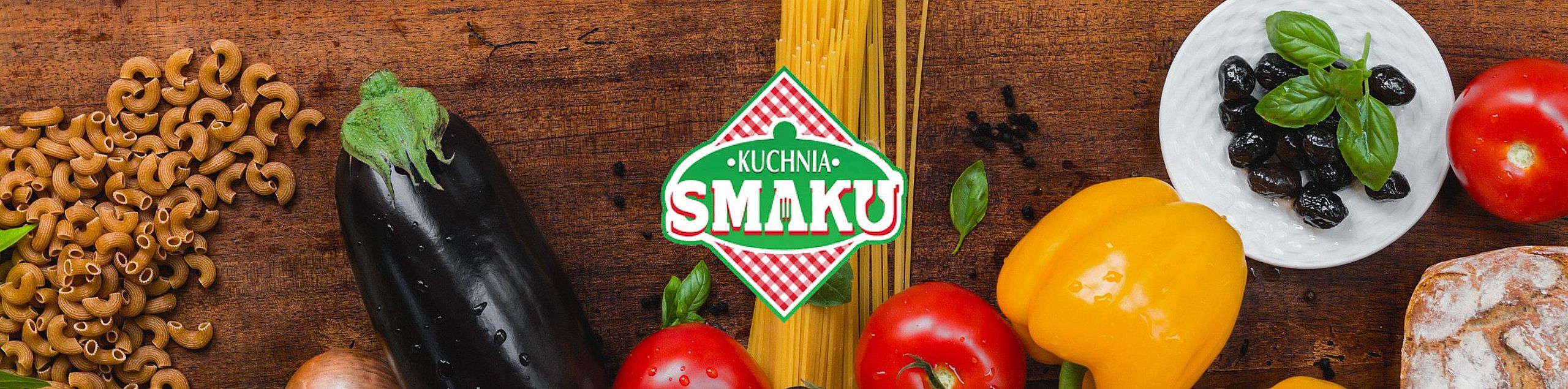 Drewniany blat kuchenny pełen kolorowych, świeżych składników: makaron, bakłażan, pomidory, papryka, czarne oliwki, cebula i pieczywo. W centrum znajduje się logo „Kuchnia Smaku” na tle czerwono-białej kraty w kształcie rombu.