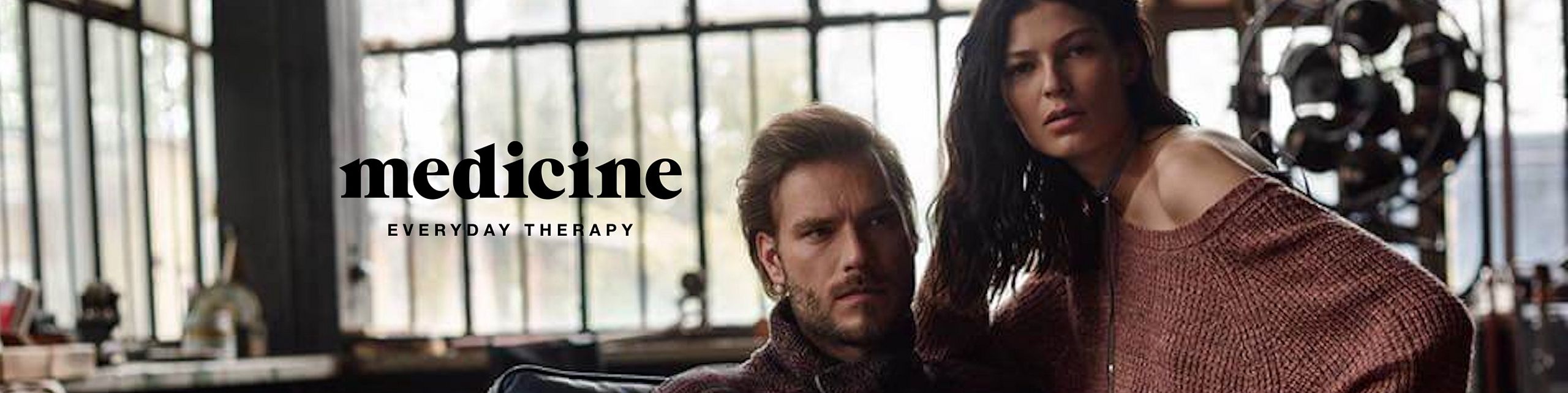 Para w jesienno-zimowych stylizacjach marki Medicine, w klimatycznym, industrialnym wnętrzu z dużymi oknami. Po lewej stronie logo „medicine – everyday therapy”.