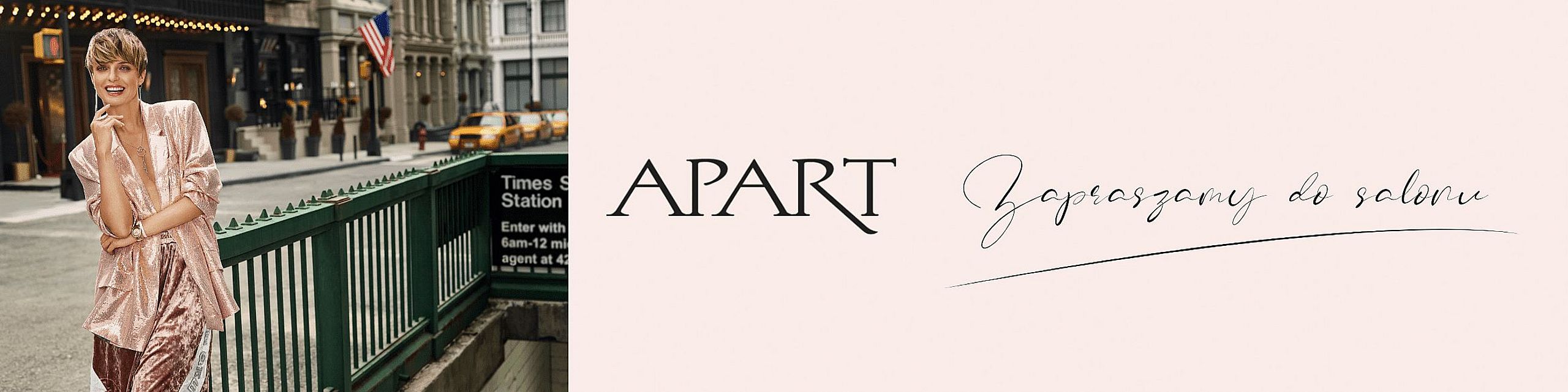 Uśmiechnięta kobieta w eleganckim, różowym stroju stoi przy wejściu do stacji metra Times Square w Nowym Jorku. Po prawej stronie widoczne logo marki "APART" i napis "Zapraszamy do salonu".