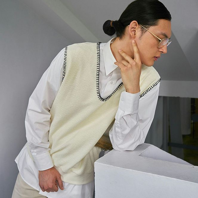 Model in a white shirt and light vest leaning on a railing.