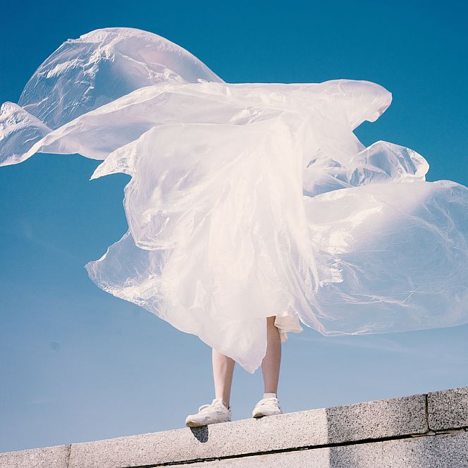 Person wrapped in flowing white fabric against a blue sky