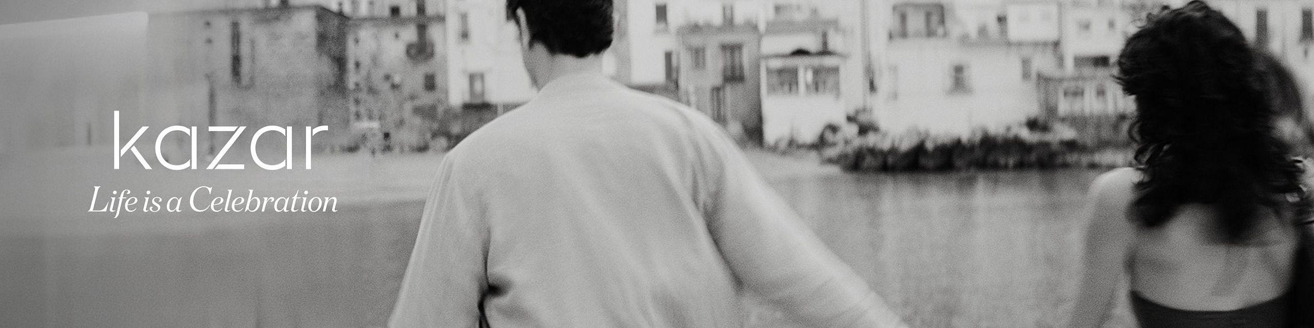 Black-and-white photo of a couple holding hands by the water, with the text “kazar – Life is a Celebration.”