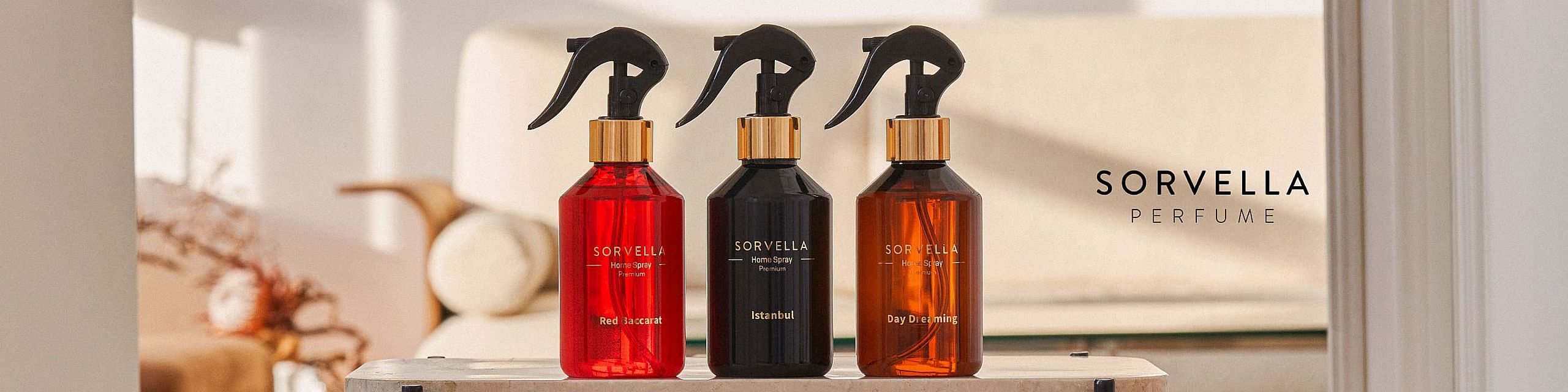 Trzy butelki sprayów do domu Sorvella – Red Baccarat, Istanbul i Day Dreaming – ustawione na stole w przytulnym, słonecznym wnętrzu.