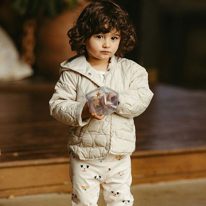 Toddler in a light jacket holding a plastic container.
