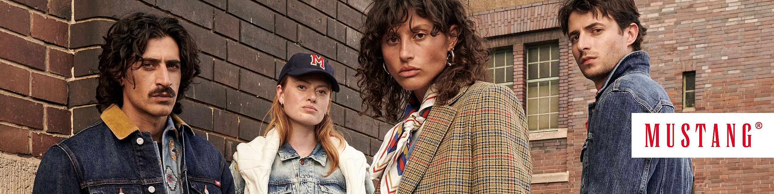 Czworo młodych osób pozuje w miejskiej scenerii przy ceglanej ścianie, ubranych w stylowe ubrania marki Mustang, w tym jeansowe kurtki, marynarkę i czapkę z literą M. Po prawej stronie widoczne logo marki Mustang.