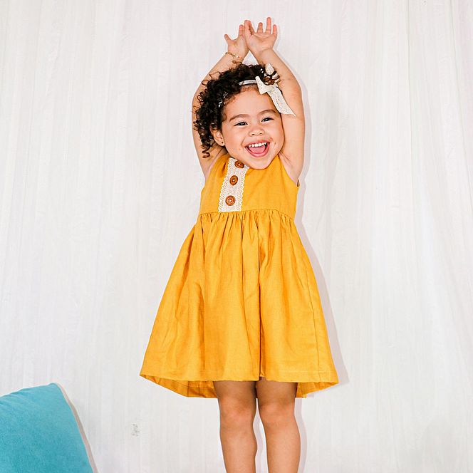 Smiling girl in a yellow dress with raised arms.