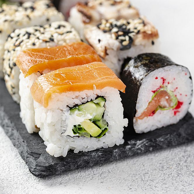 Zbliżenie na zestaw różnorodnych kawałków sushi ułożonych na kamiennej desce.