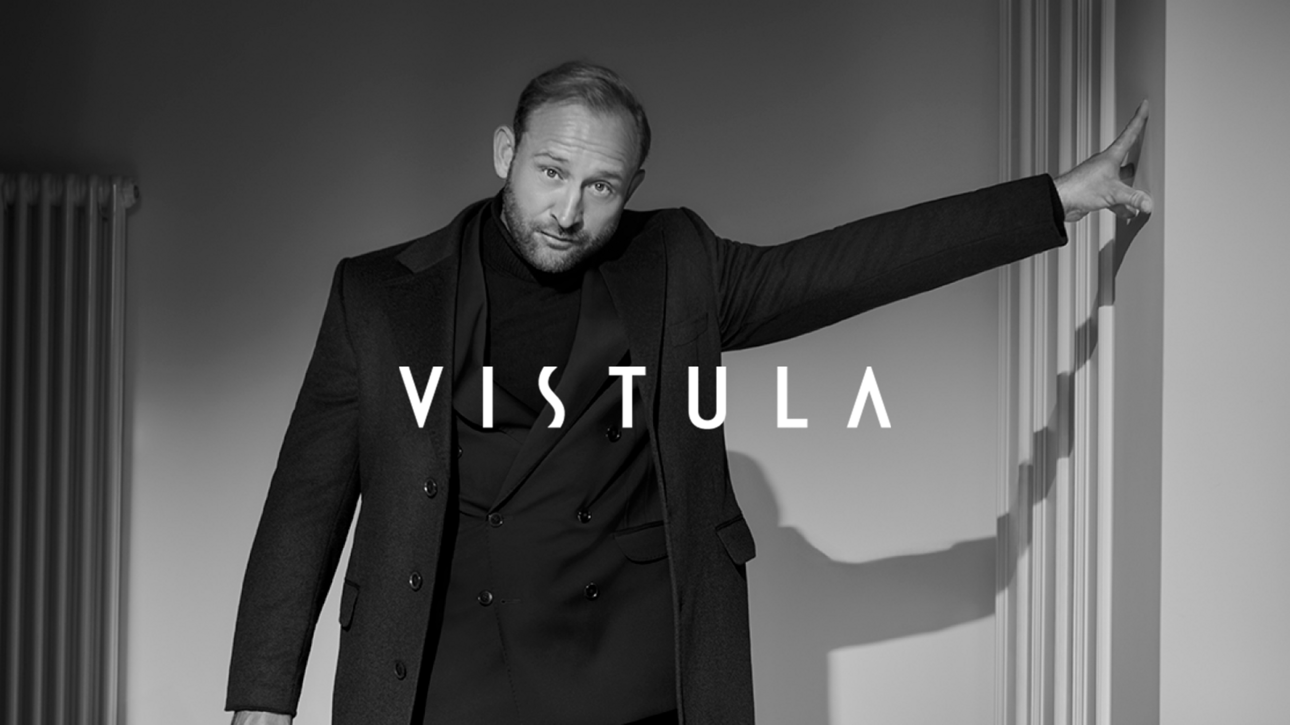A man in an elegant black Vistula outfit in a black-and-white setting.