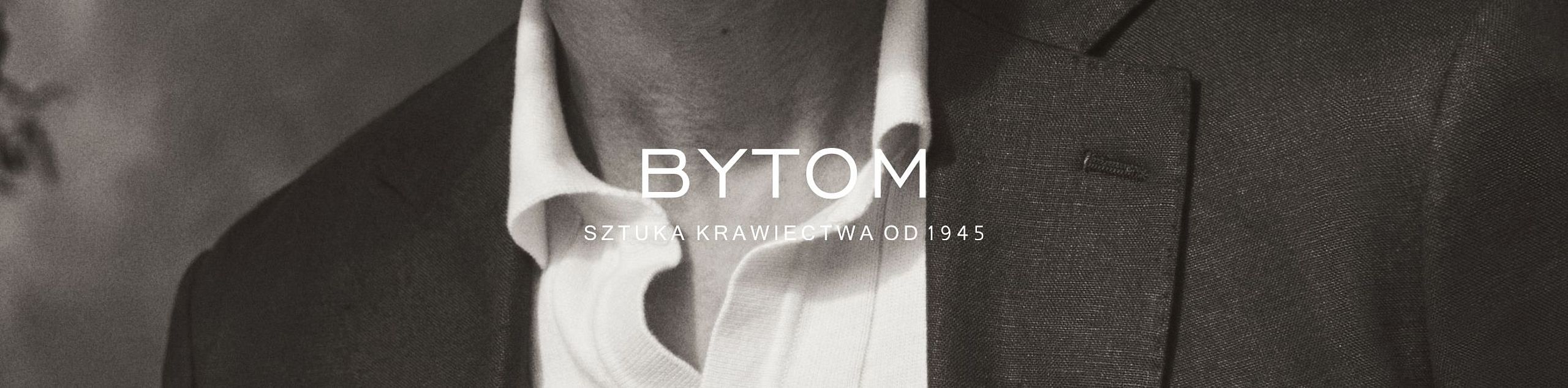 Zbliżenie na elegancki męski garnitur i koszulę z logo BYTOM oraz napisem 'Sztuka krawiectwa od 1945' na środku obrazu.