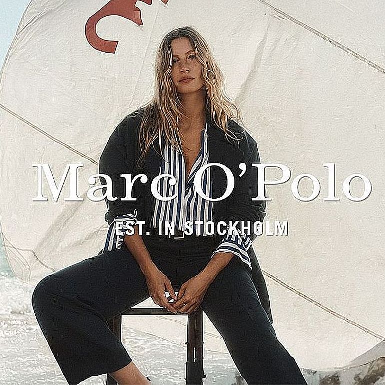 Modelka w eleganckim, casualowym stroju marki Marc O’Polo, siedząca na krześle na tle żagla nad morzem. Na zdjęciu widoczne logo Marc O’Polo oraz napis „EST. IN STOCKHOLM”.