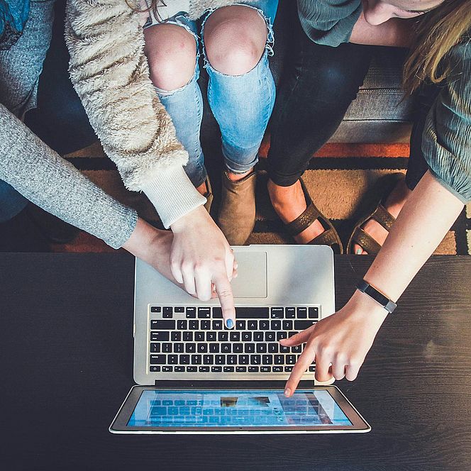 Group of people pointing at a laptop screen while working together