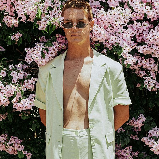 Man in a light suit standing in front of pink flowers.