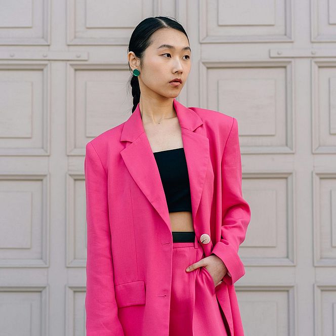 Female model in a pink suit standing in front of light-colored doors.