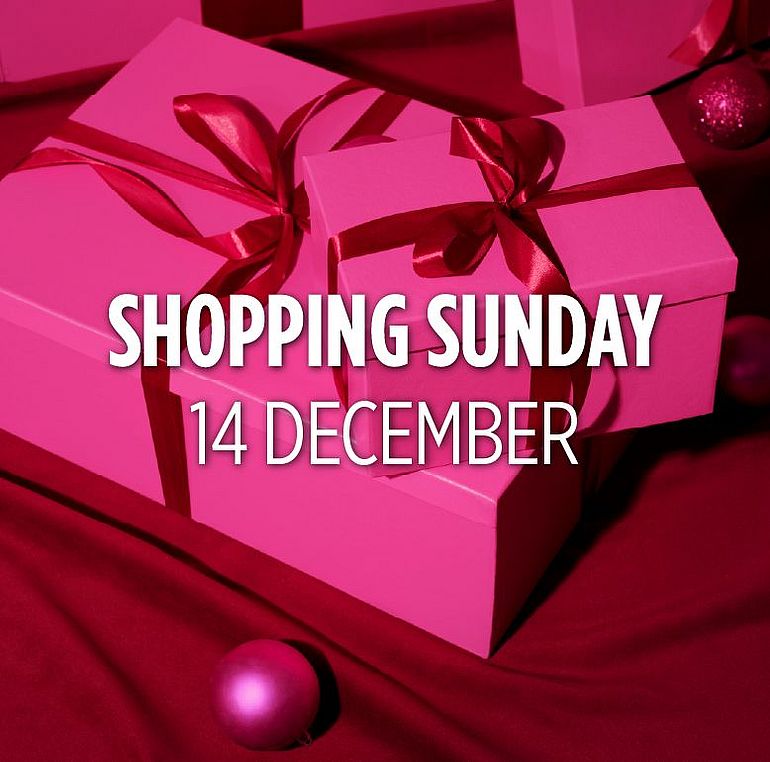 A woman in a pink dress holding a purple bauble, with gifts in the background.