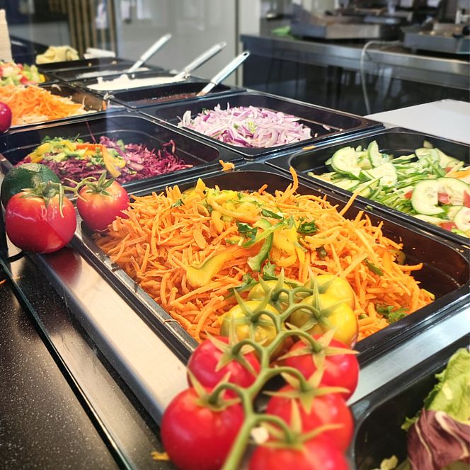  Kebab z kolorowymi warzywami: startą marchewką, papryką, ogórkiem, czerwoną kapustą i pomidorami na gałązce, ustawiony w metalowych pojemnikach