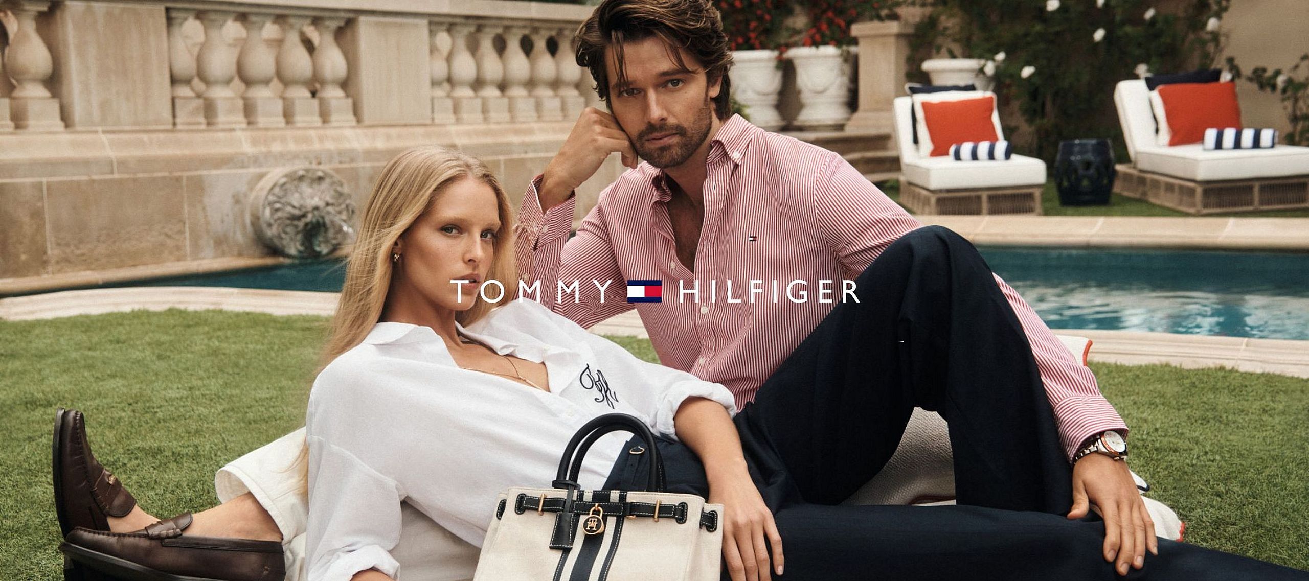 A couple relaxes on a poolside lounger in elegant summer outfits.