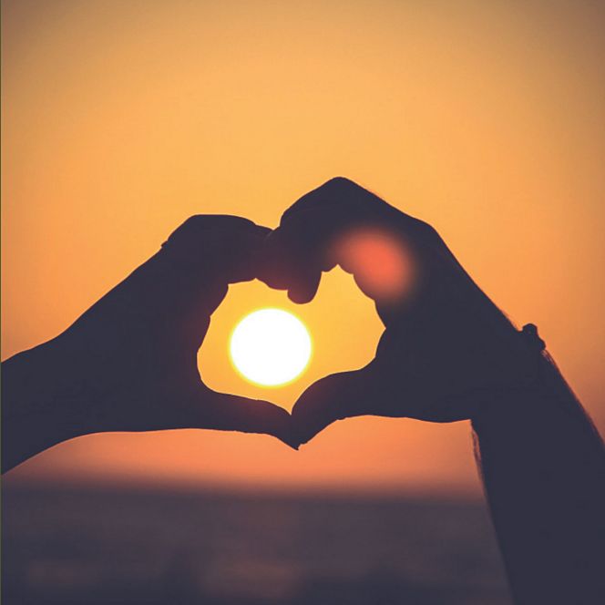 Hands forming a heart shape against the sunset