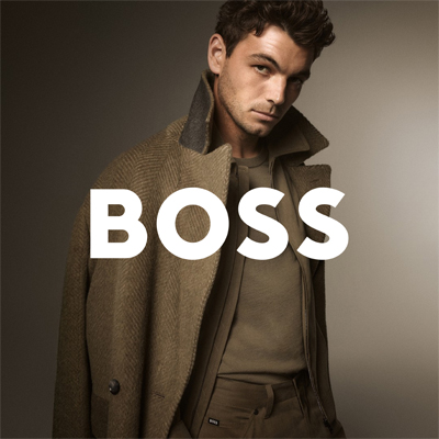 Mężczyzna w długim, eleganckim płaszczu w odcieniach brązu patrzy w stronę aparatu; po prawej stronie znajduje się logo ‘BOSS’.