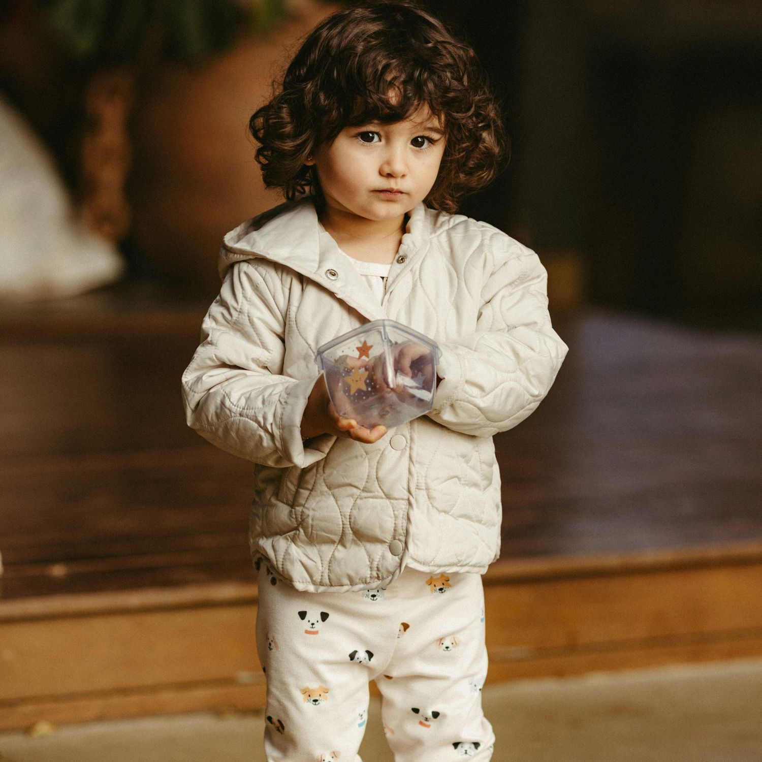 Małe dziecko w jasnej kurtce trzymające plastikowy pojemnik.
