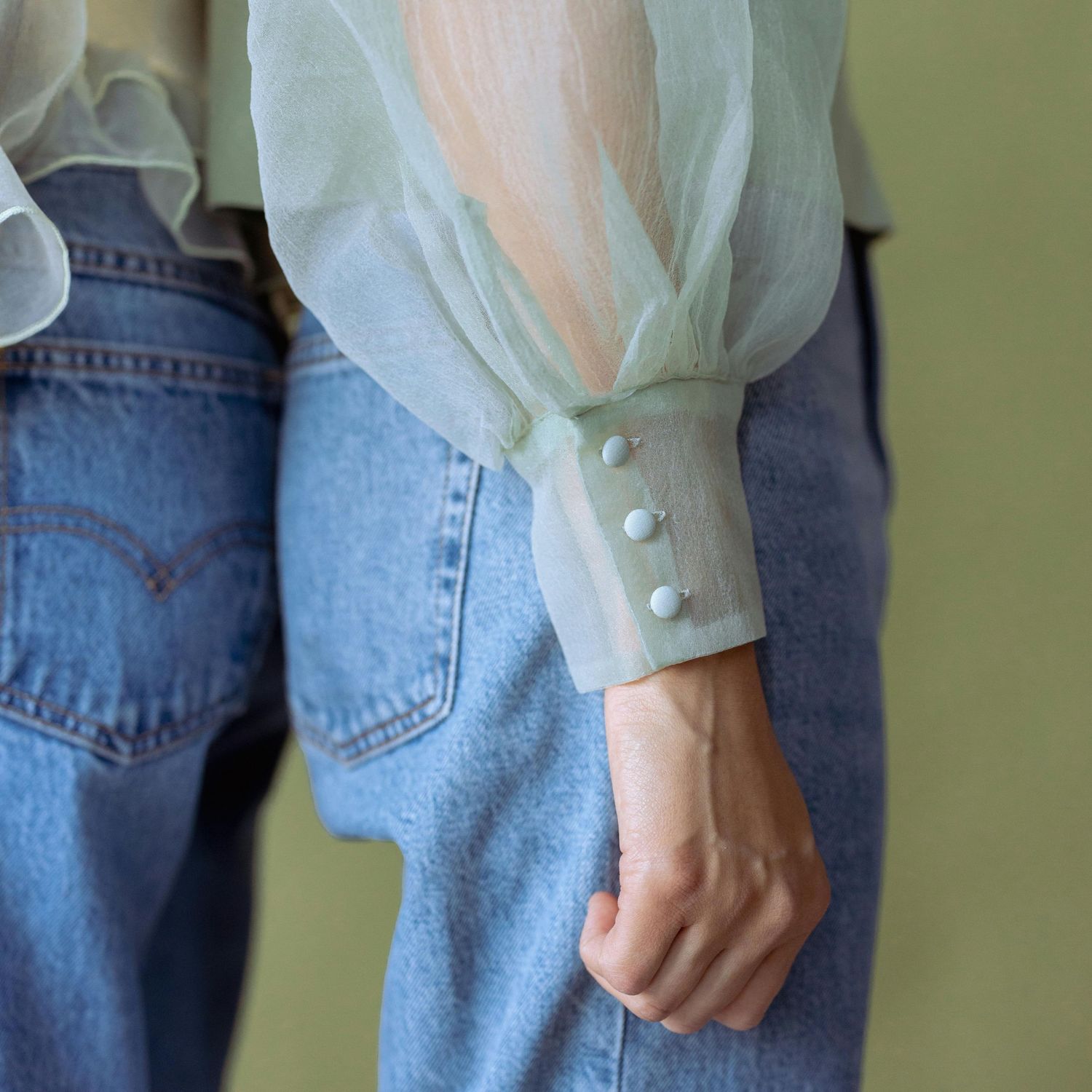 Zbliżenie na rękaw bluzki z guzikami i jeansy.