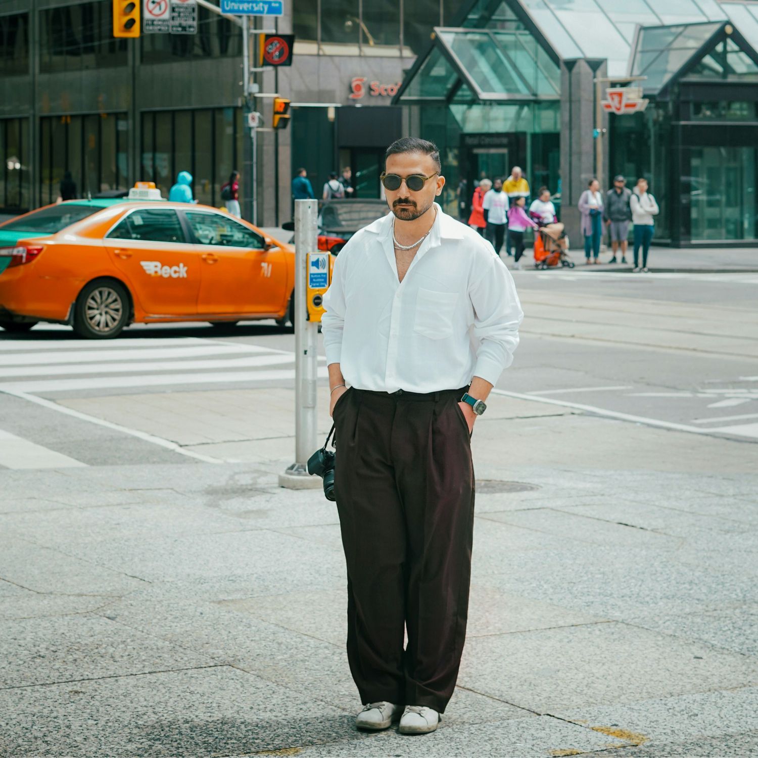 Mężczyzna w jasnym garniturze stojący przed różowymi kwiatami.