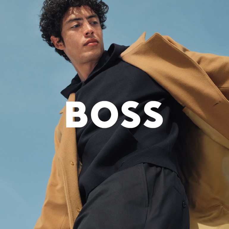 Man in a beige coat and dark sweater posing against the sky – BOSS fashion campaign.