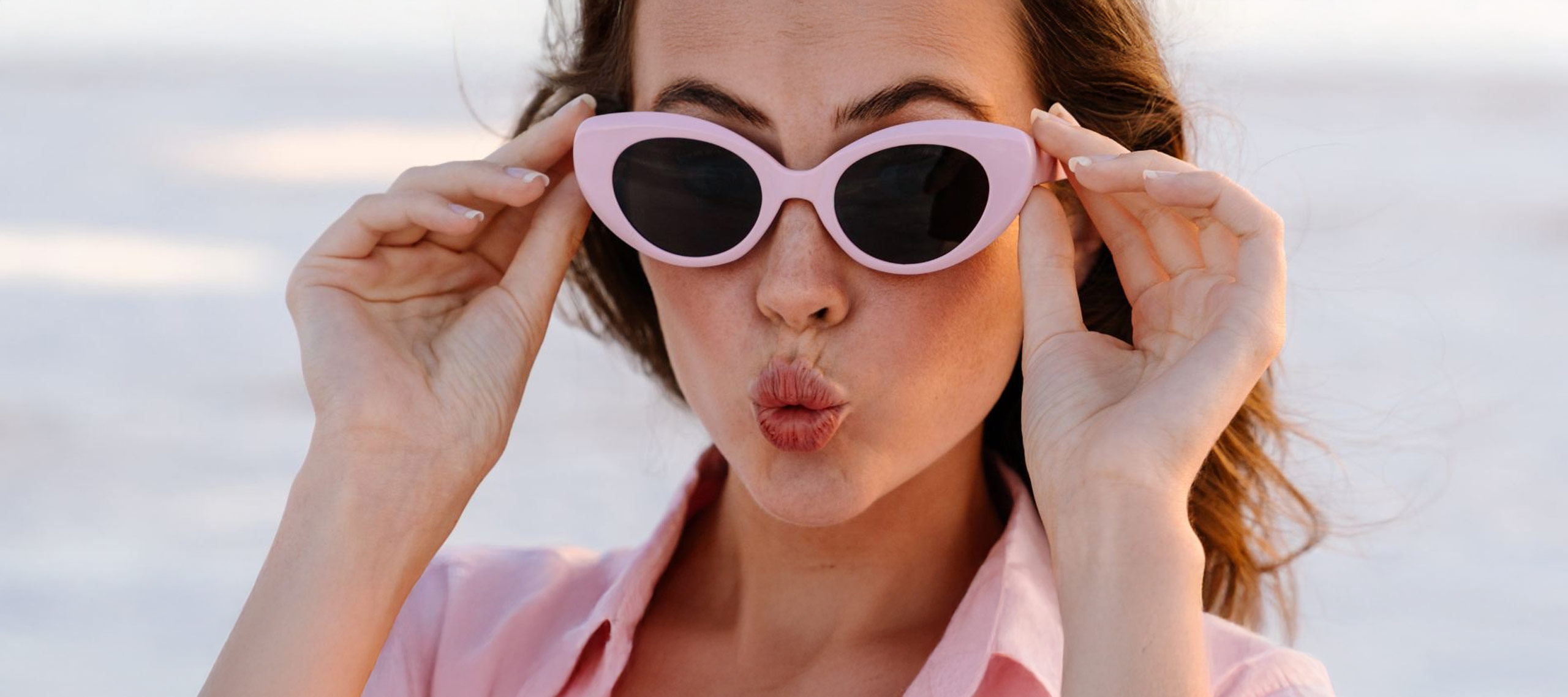 Kobieta w różowych okularach przeciwsłonecznych robiąca zabawną minę i poprawiająca oprawki.