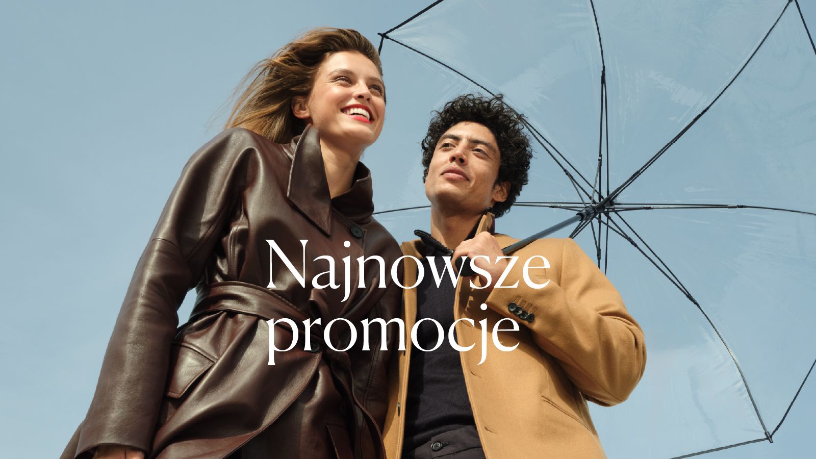 Para w eleganckich jesiennych stylizacjach pod parasolem na tle błękitnego nieba.