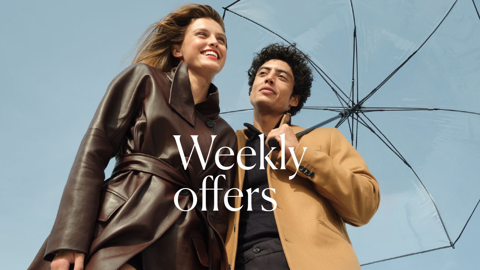 A couple in elegant autumn outfits under an umbrella against a blue sky.