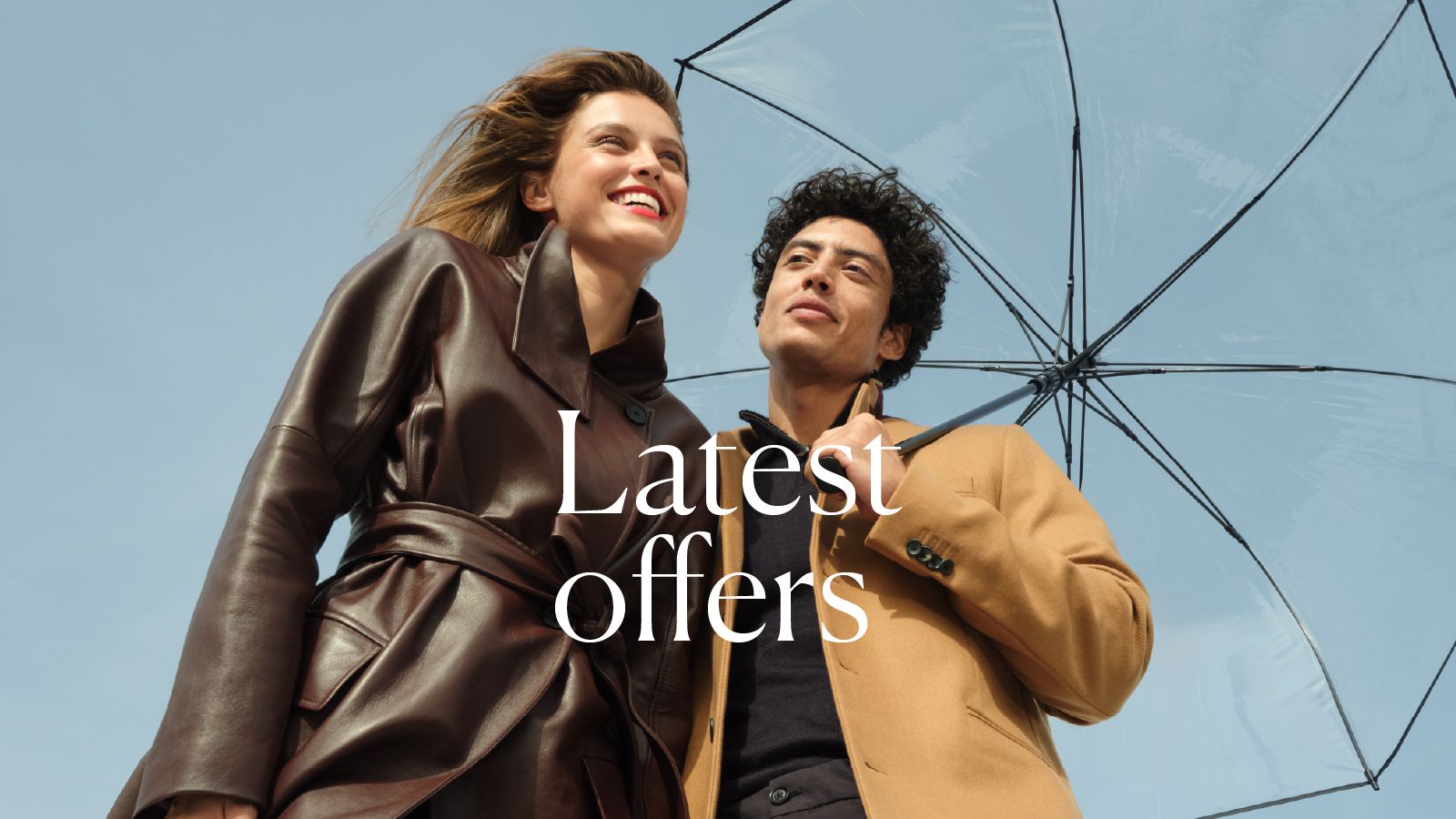A couple in elegant autumn outfits under an umbrella against a blue sky.