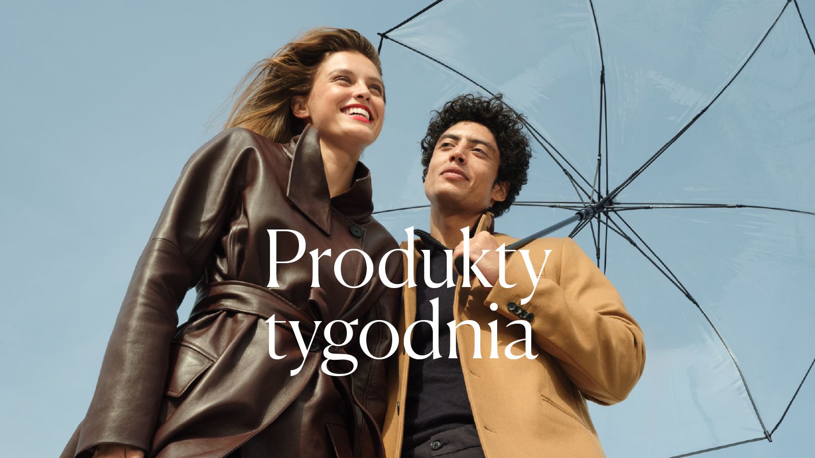 Para w eleganckich jesiennych stylizacjach pod parasolem na tle błękitnego nieba.