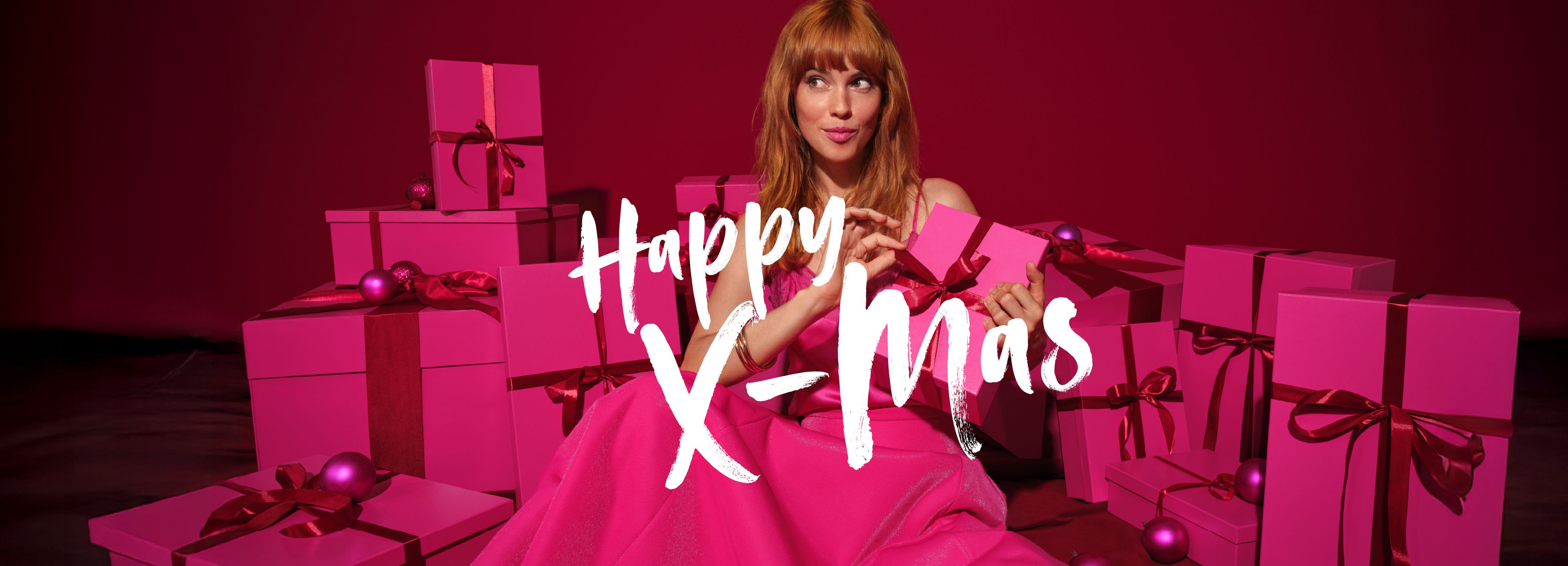 A woman in a pink dress among pink gifts on a red background, with the inscription “Happy X-Mas”
