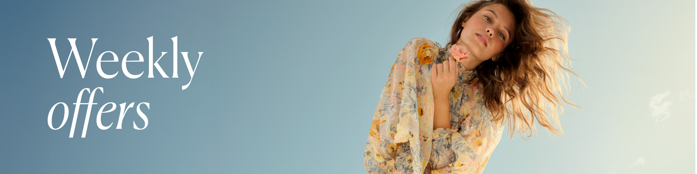 A woman in a light, floral dress holding a delicate pale pink flower near her face.