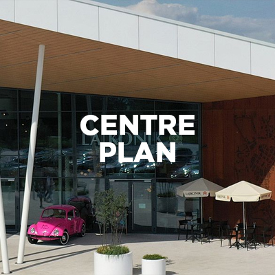 Entrance to a shopping center with the text PLAN CENTRUM, a pink car and café tables nearby.