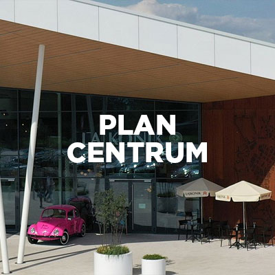 Wejście do centrum handlowego z napisem PLAN CENTRUM, obok stoi różowy samochód i stoliki kawiarni.
