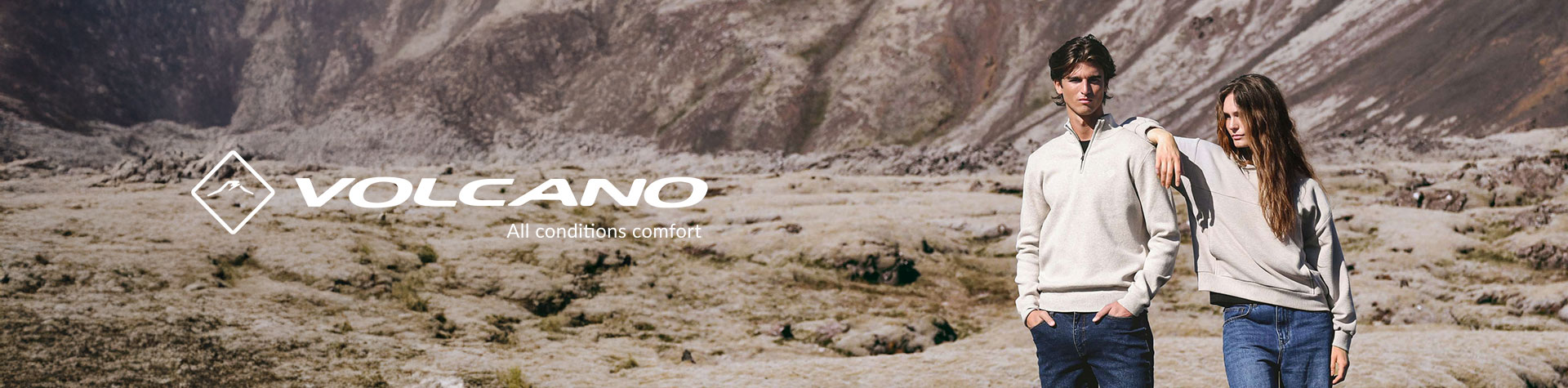 Para młodych ludzi w jasnych swetrach i dżinsach stoi na tle skalistego, górskiego krajobrazu; obok logo marki VOLCANO i hasło 'All conditions comfort'.