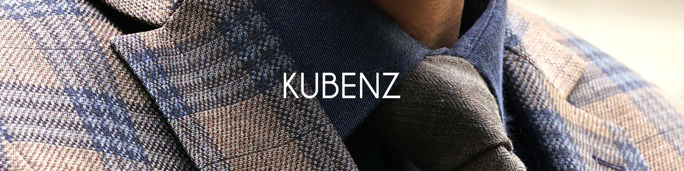 Zbliżenie na elegancki męski strój – krawat, koszula w ciemnym odcieniu i marynarka w kratę w odcieniach niebieskiego i beżu. Na środku widnieje białe logo „KUBENZ”.